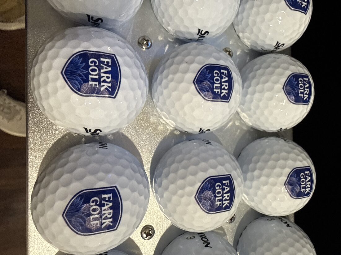Close-up of premium golf balls printed with the navy FARK Golf crest logo