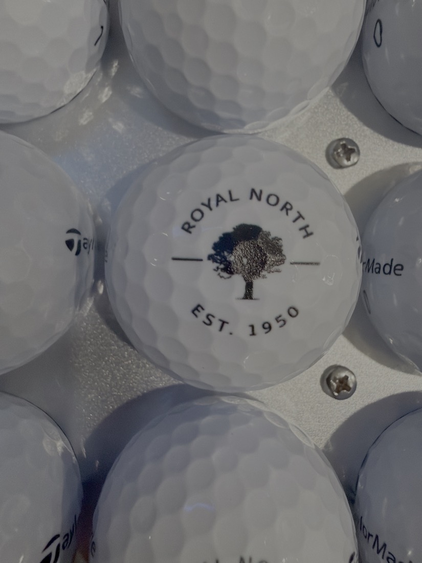 Close-up of a TaylorMade golf ball printed with the Royal North golf club crest — a tree above 'EST. 1950'